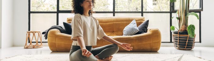 Young multiracial latina woman meditating at home with online video meditation lesson using laptop. Meditation and spirituality concept.