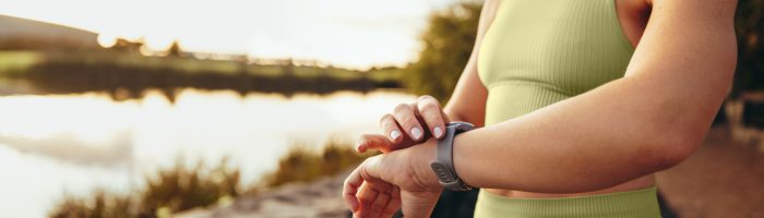 Fit woman checking her heart rate on a smartwatch outdoors. Sports woman working out in the morning. Woman using a wearable computer to monitor her fitness progress.